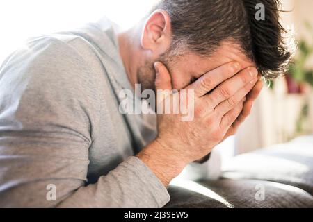 L'uomo depresso a casa sul divano sembra triste Foto Stock