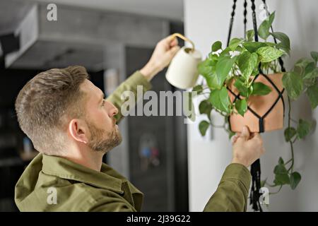 Un bell'uomo spruzzando acqua su una pianta e un fiore casa con una bottiglia a spruzzo a casa Foto Stock