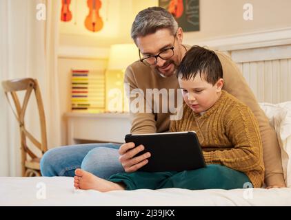 ILL ti permette di guardare un ultimo episodio prima di dormire. Girato da un padre e un figlio usando un tablet digitale insieme in una camera da letto a casa. Foto Stock