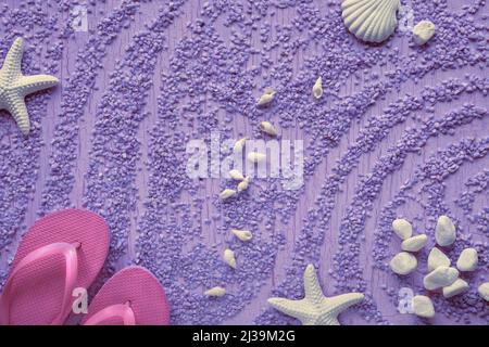 Estate al mare. Infradito in gomma magenta, pantofole su ciottoli con stelle marine, conchiglie e ciottoli, studio concept. Sfondo viola. Foto Stock