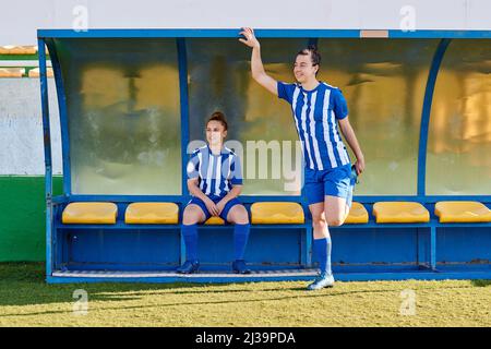 Due giocatori di calcio donne guardano fuori sopra il campo di calcio dalla panchina Foto Stock