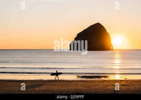 Surfisti camminando sulla spiaggia al tramonto a Pacific City, Oregon Foto Stock