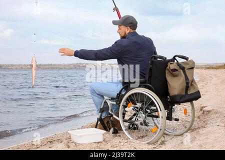 Uomo in sedia a rotelle pesca sul fiume Foto Stock