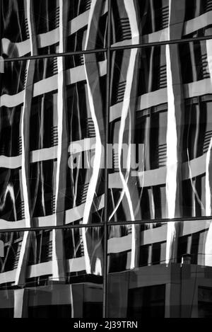 Immagine verticale in scala di grigi di un riflesso di un edificio in una superficie di vetro Foto Stock