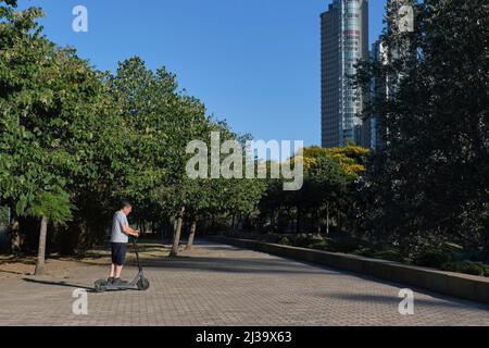 L'uomo maggiore ispanico che guida il suo scooter elettrico del calcio in città una mattinata di sole. Concetti di vita urbana attiva, mobilità moderna e trasp. Ecologico Foto Stock