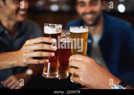 Ben meritato e pronto a bere. Primo piano di un gruppo di giovani amici seduti a un tavolo insieme mentre si gusta una birra e si festeggia con un Foto Stock