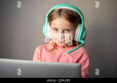 ragazza 7-8 anni indossando le cuffie, impara a guardare il webinar online, il webcast, guarda il corso di formazione a distanza su laptop o videochiama l'insegnante utilizzando Foto Stock