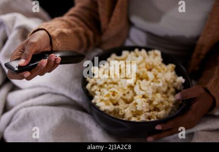 È il momento di guardare il tuo programma preferito. Ripresa ad angolo di una donna irriconoscibile che mangia popcorn mentre guardi la tv a casa. Foto Stock