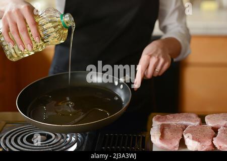 Lo chef prepara bistecche di maiale fresche in cucina, versa il burro sulla carne del menu, cucina casalinga. Ricette culinarie. Menu ristorante. Foto Stock