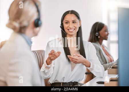 Mostrandole le corde. Scatto corto di un giovane agente di call center che indossa una cuffia e chiacchiera con un collega mentre lavora in ufficio Foto Stock