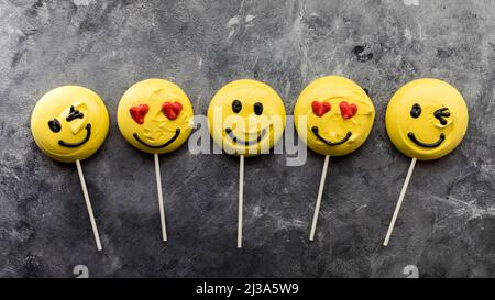 Una fila di smiley faccia Emoji merengues su lollipop bastoni. Foto Stock