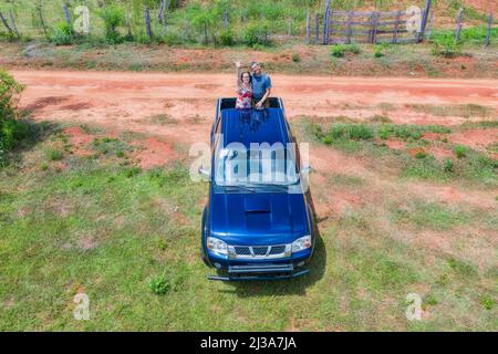 Vista aerea di una donna e di un uomo sul retro di un camion pick-up in Paraguay con tipico percorso di sabbia rossa. Foto Stock