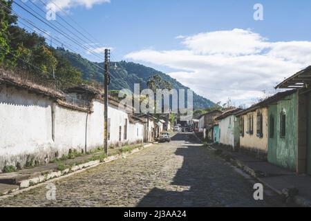 Città di Ataco a Ruta de las Flores, El Salvador. Strada vuota con marciapiede e vecchi edifici. Vista delle colline coperte di alberi in lontananza Foto Stock