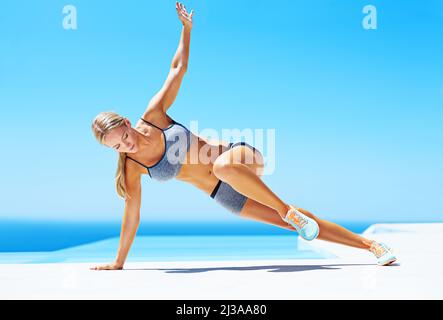 Questa è la palestra migliore di sempre. Scatto di una giovane donna che si sta allenando su un patio sotto un cielo blu. Foto Stock