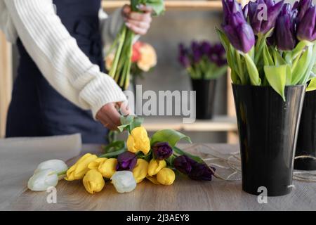 Donna fiorista crea un bouquet di tulipani gialli. Primo piano delle mani del maestro in officina prendere un bouquet. Foto Stock