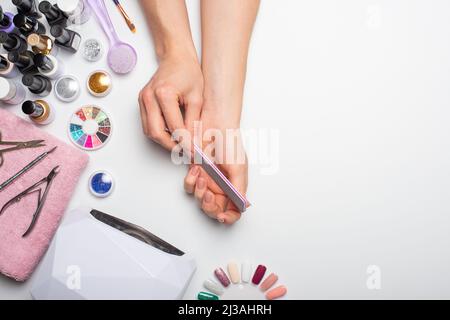 Cura delle unghie. Belle mani donne che fanno chiodi dipinti con rosa delicato smalto unghie su uno sfondo bianco. Le mani delle donne vicino ad un insieme dell'uomo professionale Foto Stock