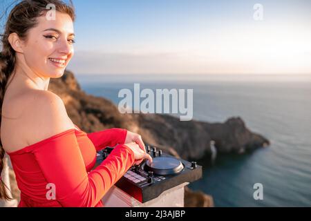 Le mani femminili del DJ suonano la musica mescolando e graffiando durante la festa serale con sfondo marino e caldo tramonto morbido. Primo piano di una console DJ controllata da Foto Stock