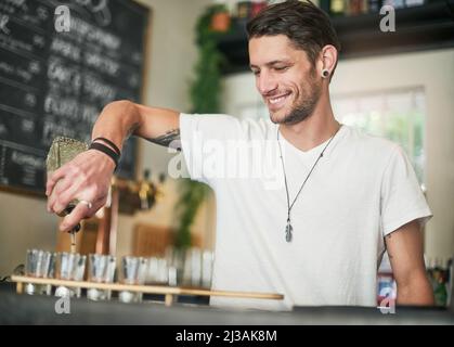 Gli sparatutto sono un antipasto istantaneo della festa. Scatto di un giovane barista felice versando colpi dietro il bar. Foto Stock