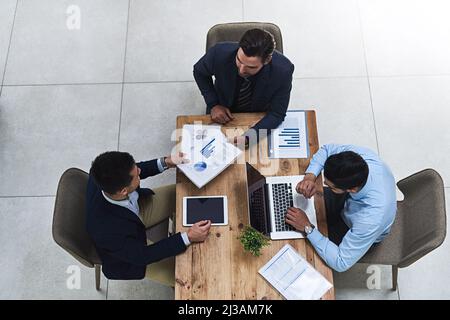 Attraverso i numeri insieme. Scatto ad alta angolazione di tre colleghi che hanno una riunione di lavoro intorno a un tavolo in ufficio. Foto Stock