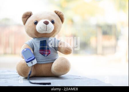 Teddy Bears seduto su un pavimento di legno utilizzando pulsossimetro FingerTIP per misurare l'ossigeno nel sangue. Concetto di salute. Foto Stock