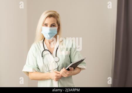 Medico femminile che indossa scrub nel corridoio ospedaliero utilizzando il tablet digitale. Foto Stock