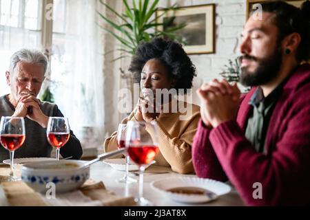 Famiglia e concetto religioso. Gruppo di persone multietniche con cibo che prega prima del pasto Foto Stock