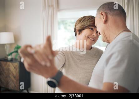 Essere tra le braccia è il mio posto preferito. Scatto di una coppia matura che balla lentamente nel loro salotto. Foto Stock