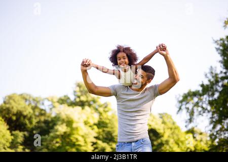 Ritratto di felice padre nero che porta la figlia sul retro all'aperto. Famiglia felicità amore concetto. Foto Stock