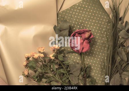 Fiori appassiti su sfondo floreale. Un bocciolo di rosa rossa e un bouquet di piccole rose gialle. Foto Stock