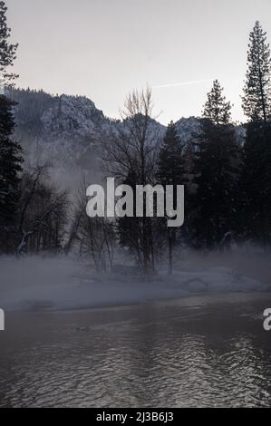 La valle di Yosemite è circondata da un sottile strato di nebbia che si estende sul fiume merced, fornendo un'atmosfera inquietante intorno al tramonto. Foto Stock