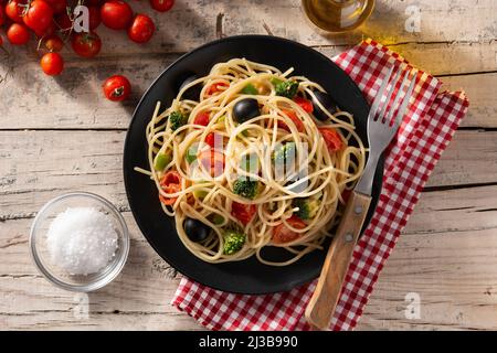 Spaghetti con verdure (broccoli, pomodori, peperoni) su tavola di legno Foto Stock