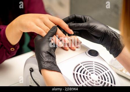 Primo piano il maestro professionale di manicure tiene la mano femminile del cliente e controlla il manicure in un salone delle unghie Foto Stock