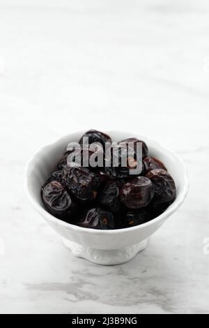 Ajwa datters on White Bowl, White Table. Aywa Date frutta popolare come Kurma Nabi, servito per Ramadan Ifthar Foto Stock