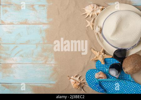 Cappello, occhiali da sole, pantofole con conchiglie e cocco e sabbia su sfondo di legno, vista dall'alto con spazio vuoto Foto Stock