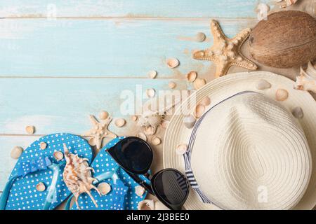 Cappello, occhiali da sole, pantofole con conchiglie e cocco e sabbia su sfondo di legno, vista dall'alto con spazio vuoto Foto Stock