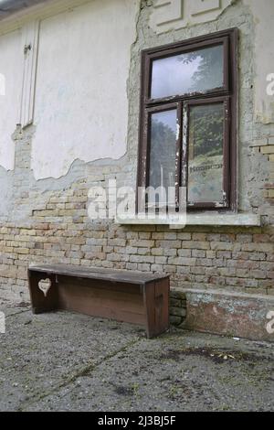 Vecchia finestra rotta con telaio in legno bianco decorativo antico dilapidato montato sulla parete della casa di famiglia incrinata. Foto Stock