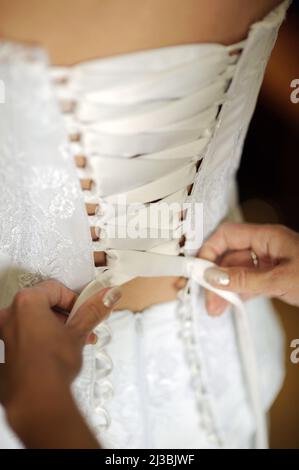 Abito da sposa corset da vicino. Preparazione della sposa. Fiocco di legatura della bridesmaid su abito da sposa. Sposa nel vestito bianco. Foto Stock