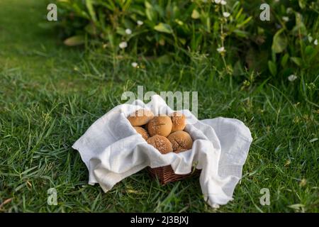 Composizione di ciambelle di farina bianca in cestello con tovagliolo bianco sull'erba verde. Foto di alta qualità Foto Stock