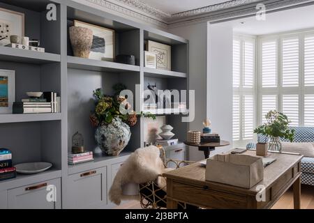 Libri e ornamenti su scaffali con persiane chiuse in casa ristrutturata St Ives, Cornovaglia, Regno Unito Foto Stock