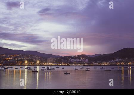 Bellissimo tramonto in tonalità rosa, blu e viola che si riflettono sul mare, nel porto di Getxo, Spagna con yacht, barche a vela e barche Foto Stock