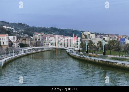 Passeggiata accanto al fiume Nervion a Bilbao (Spagna) con l'Università di Deusto su un lato e il Museo Guggenheim sullo sfondo in una giornata nuvolosa Foto Stock