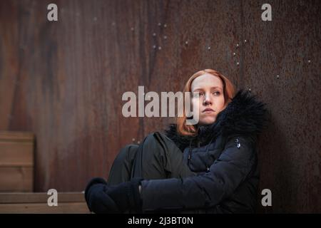 Giovane donna seduta contro il muro Foto Stock