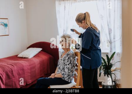 Domestico caretaker che fa i capelli della donna anziana Foto Stock