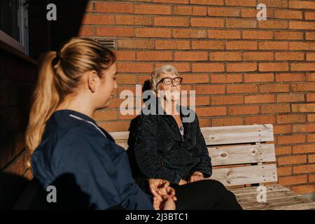 Casa custode e donna anziana seduta su panca e sole Foto Stock