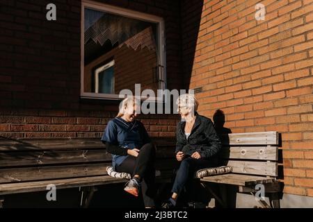 Casa custode e donna anziana seduta su panca e ridere Foto Stock