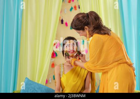 Madre che applica la pasta di curcuma sulla guancia della figlia durante la cerimonia di haldi Foto Stock