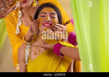 Le mani femminili applicano la pasta curmerica sul viso della sposa su haldi rasam Foto Stock