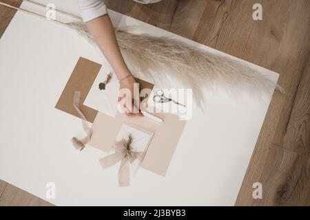 Vista dall'alto della composizione di fogli di carta, forbici, busta con sigillo di cera grigia, arco di nastro di inchiostro e erba rampas. Foto Stock