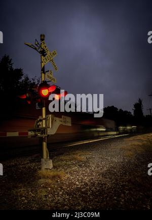 Un colpo verticale di un cancello di attraversamento della ferrovia e di un treno in movimento al crepuscolo Foto Stock