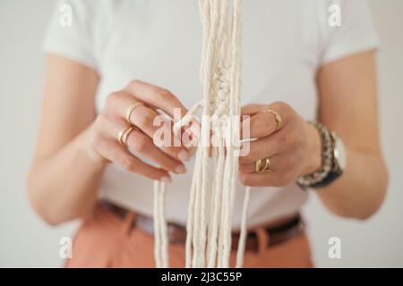 Le mani delle donne tessono un portavetrini di fiori in macrama modello in stile Boho. Foto Stock